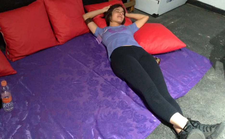 A mana Bacolou deitada sobre um lenço roxo e almofadas vermelhas.
